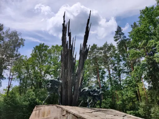 Pomnik w lasach janowskich. Grupa ludzi biegnie w stronę wysokiego, poszarpanego monumentu.