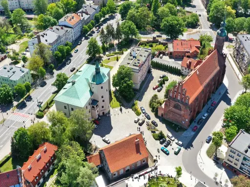 Słupsk atrakcje: zamek Książąt Pomorskich z zielonym dachem i ceglany kościół. W tle budynki mieszkalne i drzewa.