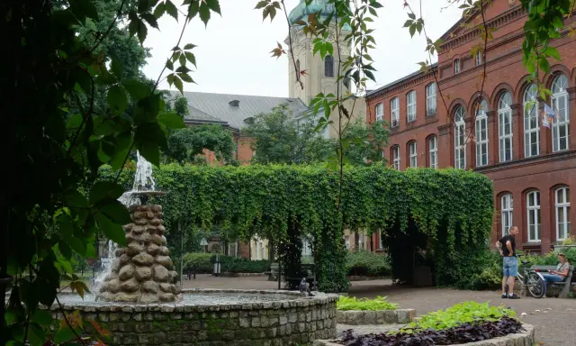 Fontanna i zielone arkady w parku miejskim, w tle zabytkowa architektura. Leszno atrakcje zachęcają do odpoczynku.