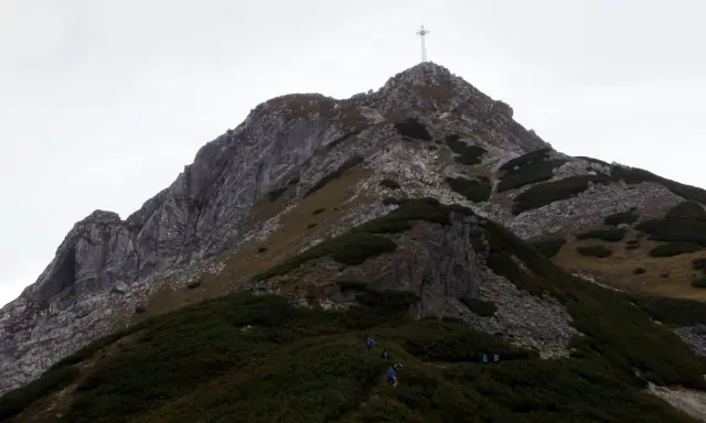 Grupa turystów wspina się na szczyt Giewontu, gdzie widoczny jest krzyż. Wjazd na Giewont to wyzwanie dla każdego miłośnika gór.