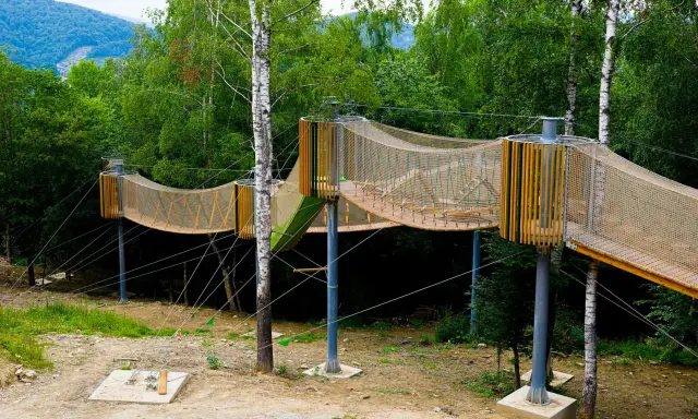Drewniana, siatkowa kładka zawieszona między drzewami, idealna na przygodową solina plaża dla dzieci.