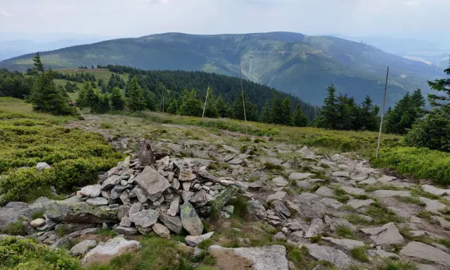 Kamienista ścieżka prowadzi przez zielone zbocza. W oddali widać pasmo górskie, które przypomina krajobraz z Lądka Zdroju.