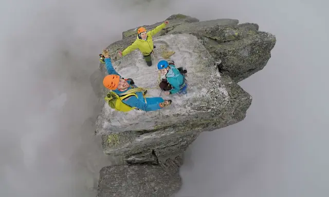 Trzech wspinaczy na szczycie Mnicha w Tatrach, otoczonych mgłą. Radość i adrenalina na twarzach.