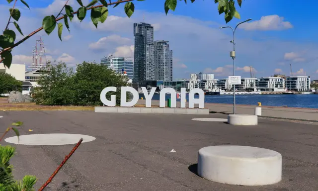 Napis GDYNIA na tle nowoczesnej architektury i żaglowca. Odkryj atrakcje Gdyni!