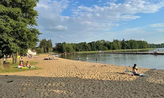 Słoneczna plaża w Insku z ludźmi odpoczywającymi na piasku i kąpiącymi się w jeziorze.