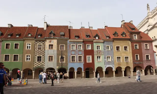 Kolorowe kamienice na Rynku w Poznaniu, sercu Polski. Ludzie spacerują po brukowanym placu.