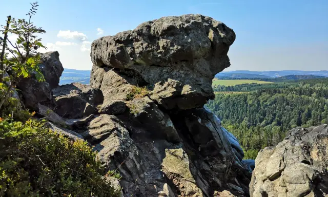 Wielkie, szare skały na szczycie góry, z których roztacza się widok na zielone lasy i pola.