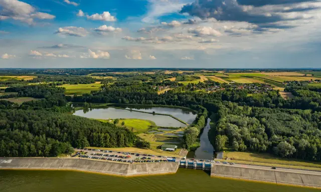 Malowniczy krajobraz z jeziorem Chańcza, zaporą, lasami i polami uprawnymi pod błękitnym, chmurowym niebem.