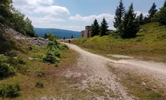 Droga na Wysoką Kopę. Kręty szlak prowadzi przez zielone wzgórza, w oddali widać budynek i góry.