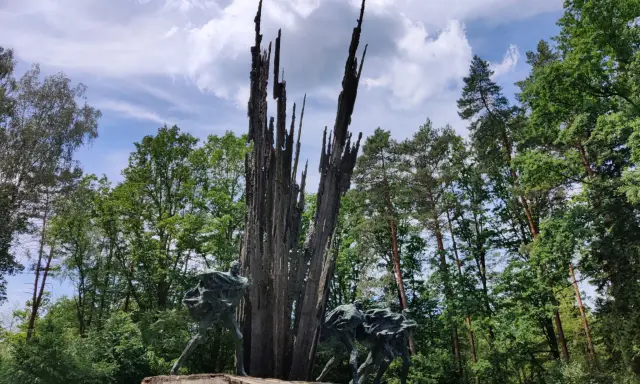 Pomnik w lasach janowskich. Grupa ludzi biegnie w stronę wysokiego, poszarpanego monumentu.
