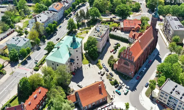 Słupsk atrakcje: zamek Książąt Pomorskich z zielonym dachem i ceglany kościół. W tle budynki mieszkalne i drzewa.