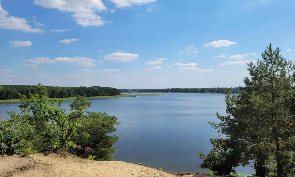 Piękny, spokojny dzień nad jeziorem Maziarnia. Błękitne niebo z białymi chmurkami, otoczone zielonym lasem.