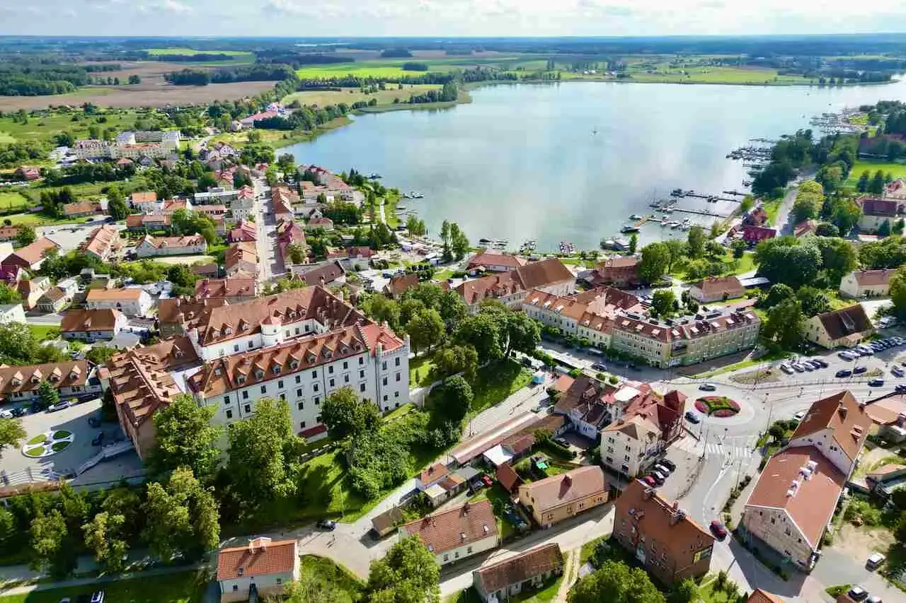 Idealne mazury na weekend: urokliwe miasteczko z zamkiem, jezioro z przystanią i zielone pola w tle.