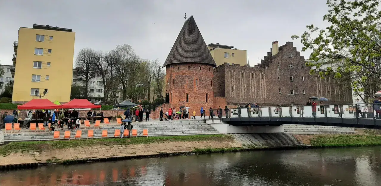Spacer po Słupsku: wieża, most z wystawą, czerwone namioty i ludzie cieszący się atrakcjami.