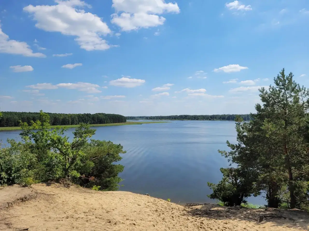 Piękny, spokojny dzień nad jeziorem Maziarnia. Błękitne niebo z białymi chmurkami, otoczone zielonymi lasami.