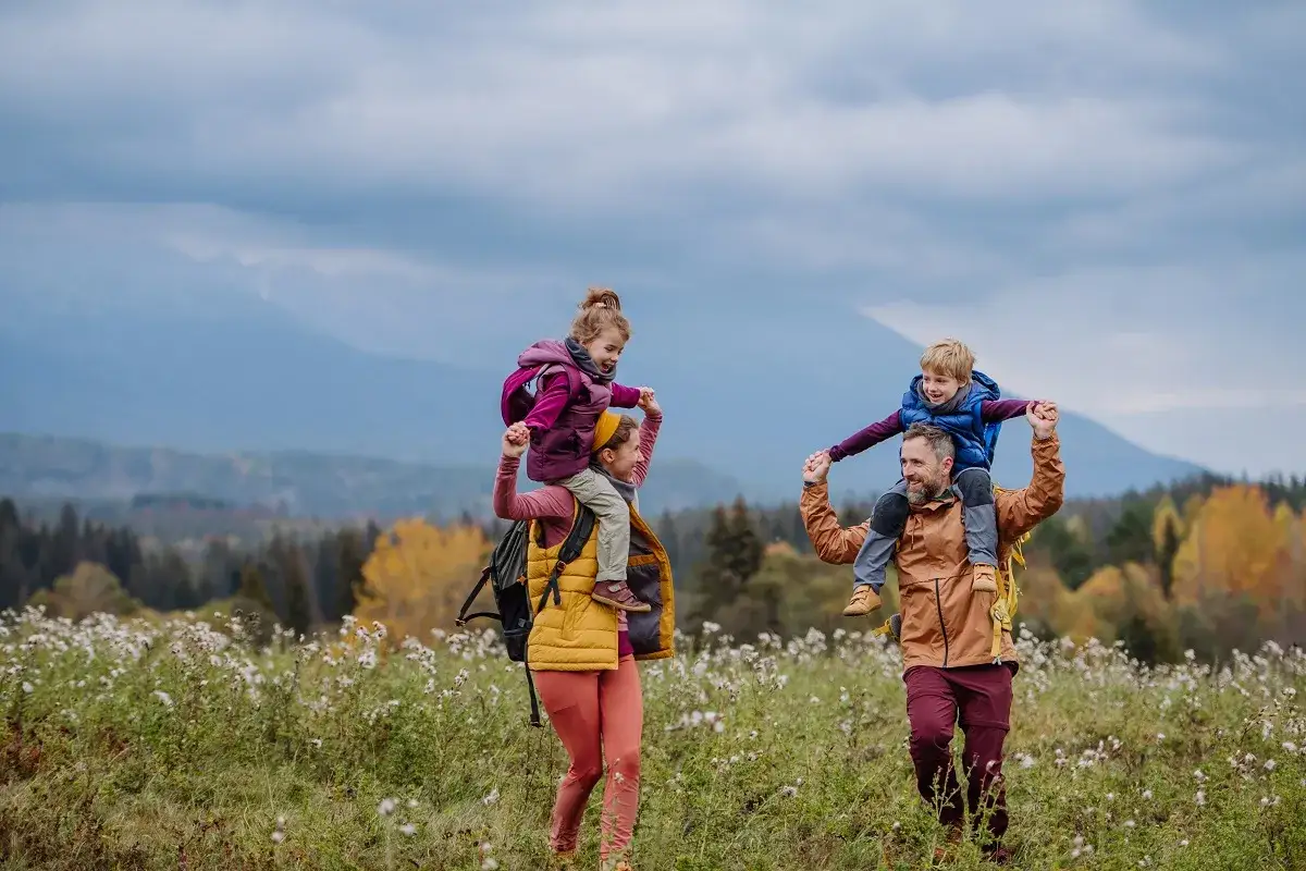Rodzina wędruje po łące z dziećmi na barana, podziwiając jesienne Tatry.