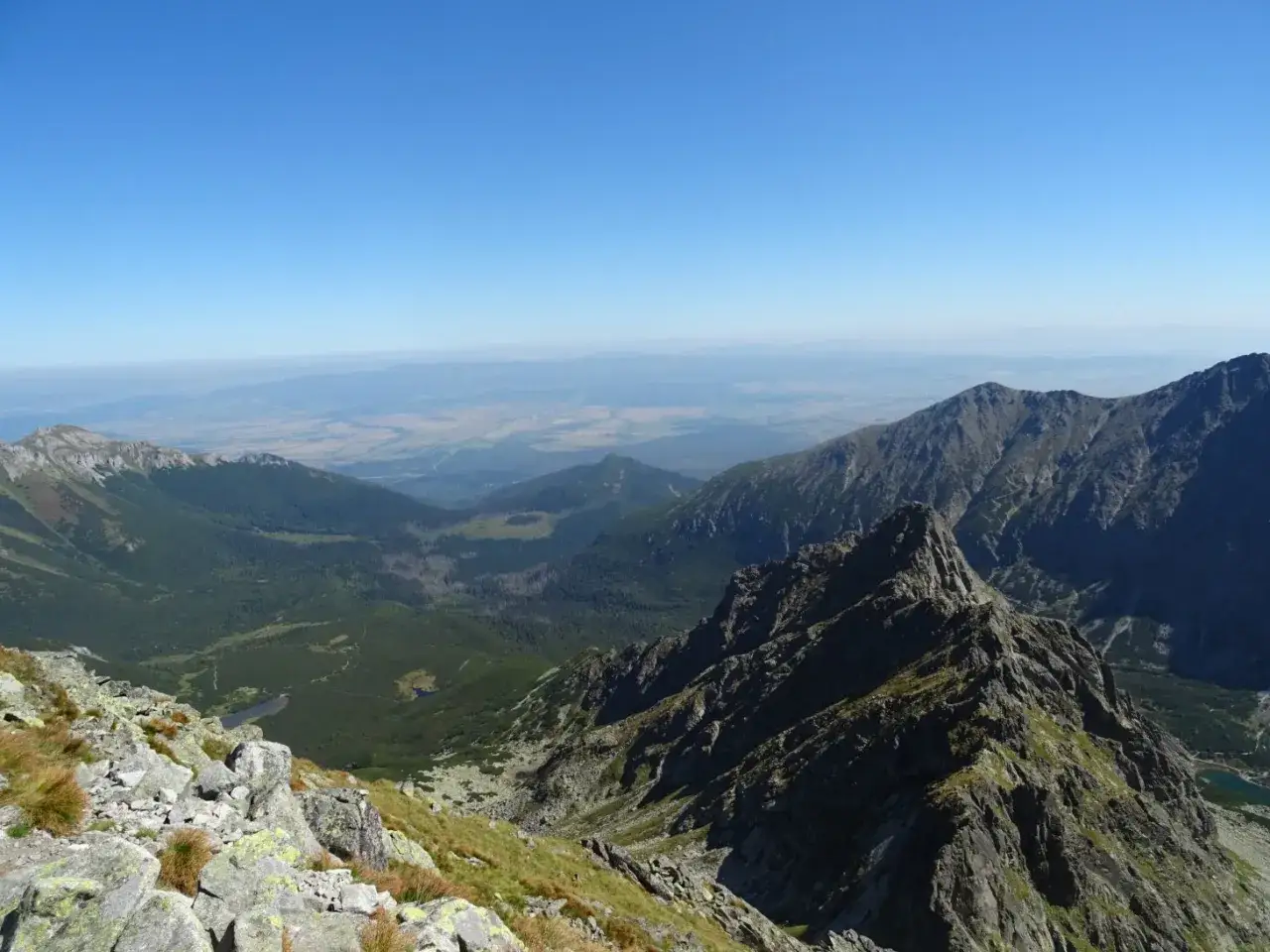 Widok z Jagnięcego Szczytu na Tatry Wysokie. Kamieniste zbocza, lasy i doliny rozciągają się aż po horyzont.