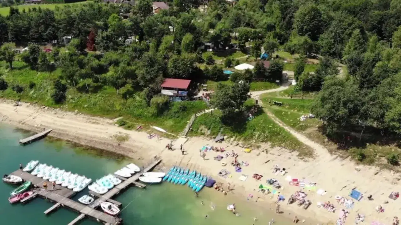 Słoneczna plaża dla dzieci z ł&oacute;dkami i kajakami na wodzie. Ludzie odpoczywają na piasku, ciesząc się latem.