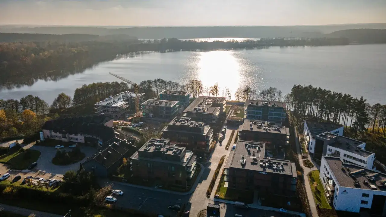 Nowoczesne osiedle nad jeziorem Ukiel, z widokiem na las i błyszczącą taflę wody.
