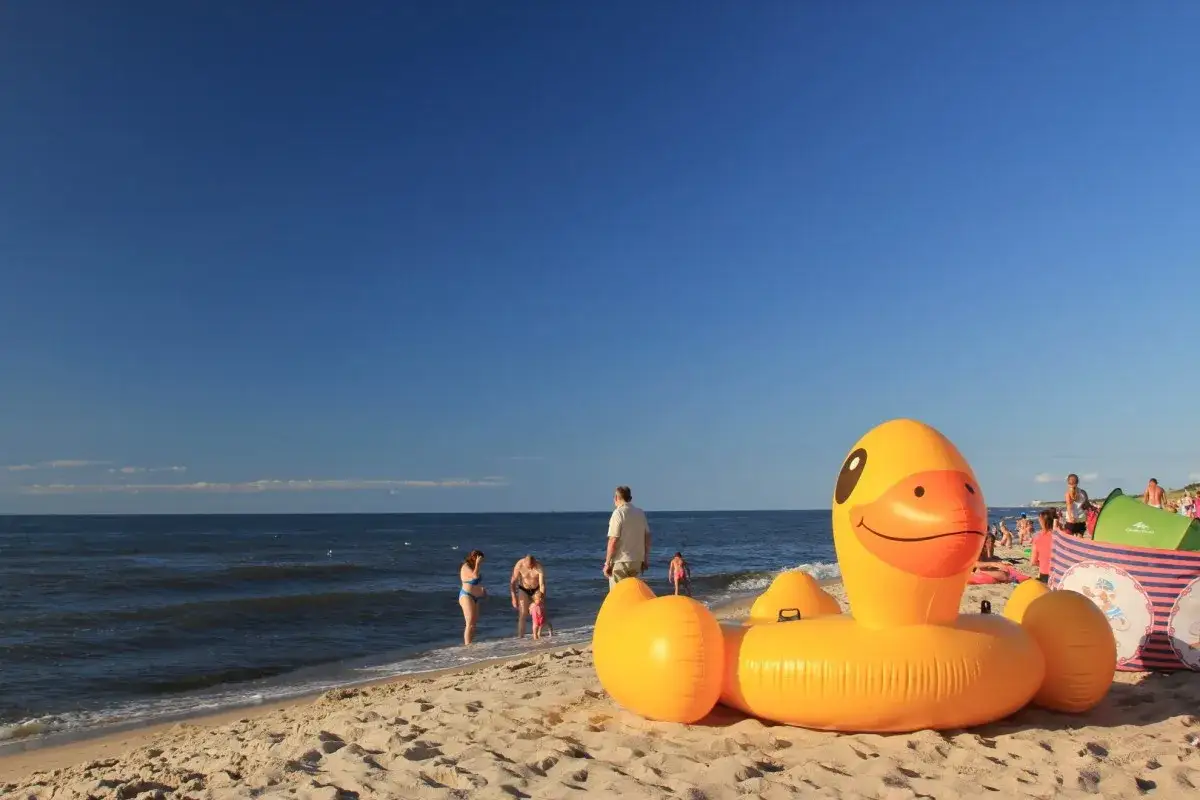 Na plaży w Bobolinie dmuchana kaczka i namioty zapowiadają świetne atrakcje dla dzieci. Rodziny kąpią się w morzu.