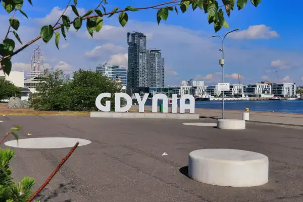 Napis GDYNIA na tle nowoczesnej architektury i żaglowca. Odkryj atrakcje Gdyni!